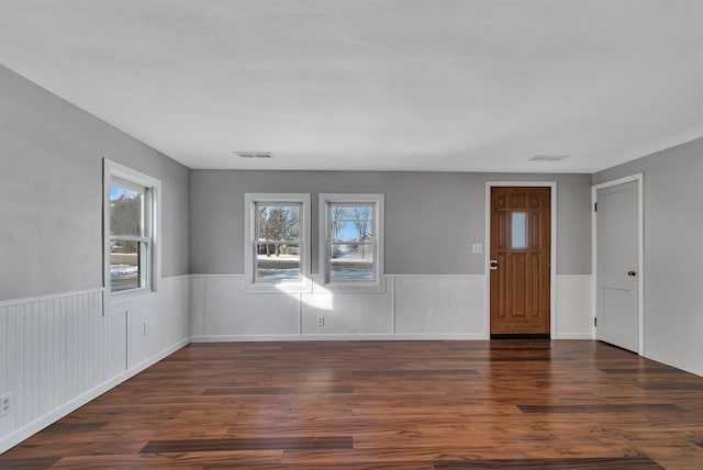 empty room featuring wood finished floors, visible vents, and wainscoting