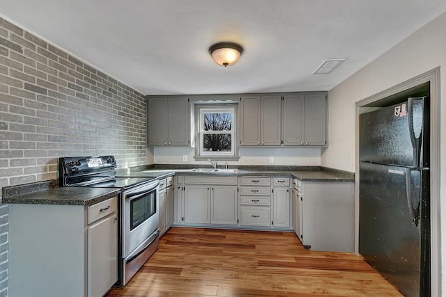 kitchen featuring stainless steel electric range oven, wood finished floors, freestanding refrigerator, a sink, and dark countertops