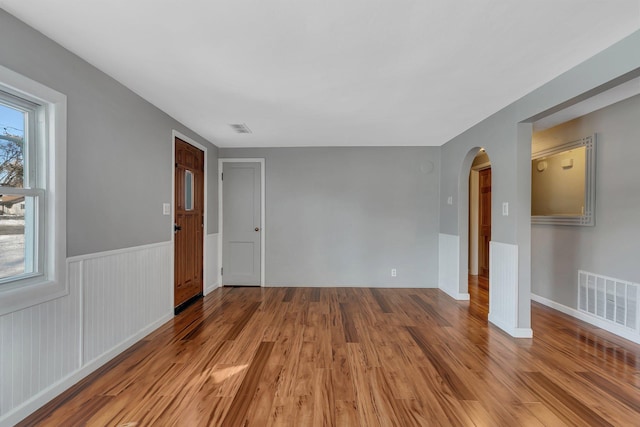 empty room featuring wood finished floors, arched walkways, and visible vents