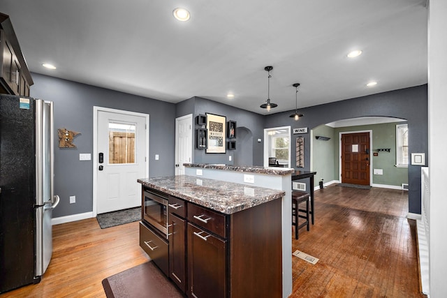 kitchen with a kitchen bar, hanging light fixtures, a center island, stainless steel appliances, and dark brown cabinets