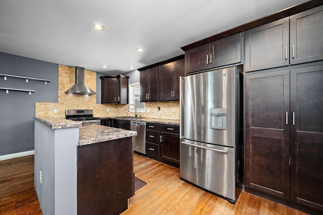 kitchen featuring sink, light stone counters, appliances with stainless steel finishes, decorative backsplash, and wall chimney range hood