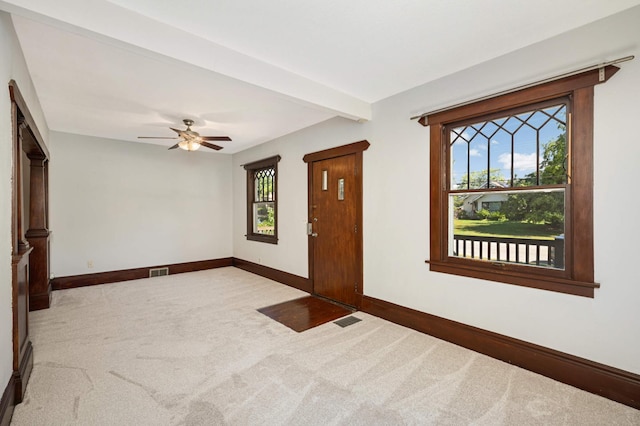 empty room with ceiling fan, a healthy amount of sunlight, beam ceiling, and light carpet