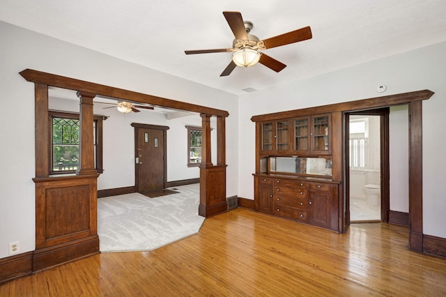 empty room featuring ceiling fan, decorative columns, and light wood-type flooring