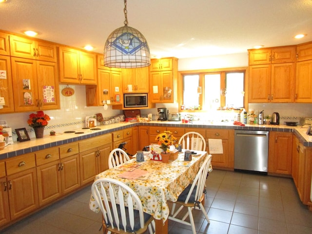 kitchen featuring appliances with stainless steel finishes, pendant lighting, tasteful backsplash, dark tile patterned flooring, and tile counters