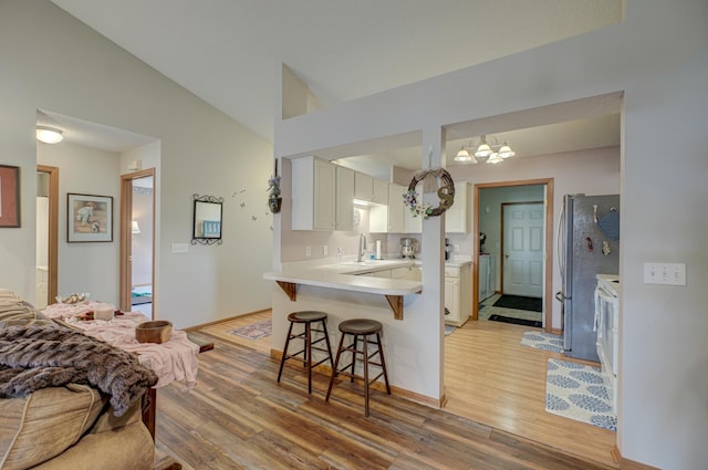 kitchen with sink, vaulted ceiling, light wood-type flooring, kitchen peninsula, and white cabinets