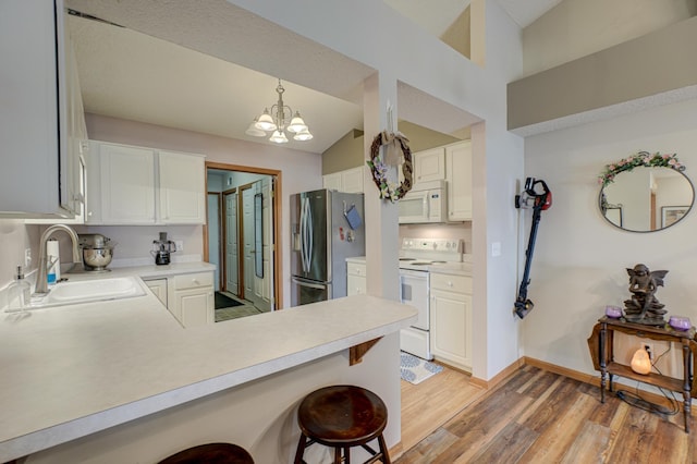 kitchen featuring sink, white appliances, hanging light fixtures, white cabinets, and kitchen peninsula