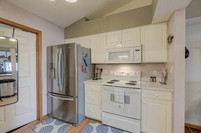 kitchen featuring white appliances, vaulted ceiling, white cabinets, and light wood-type flooring