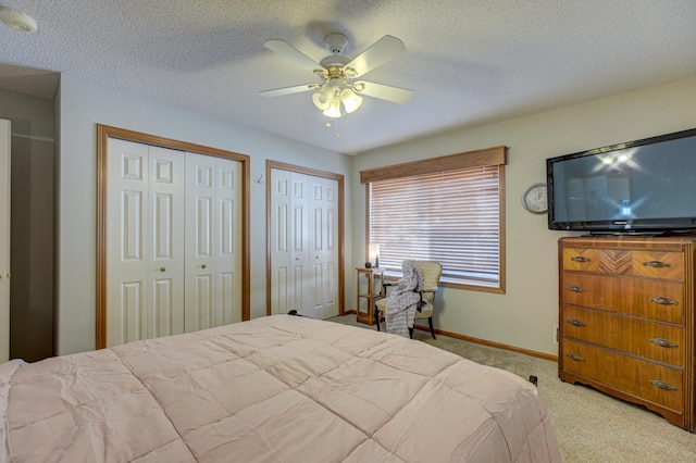 bedroom with ceiling fan, two closets, light colored carpet, and a textured ceiling