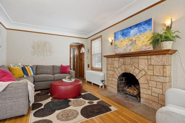 living room featuring ornamental molding, radiator, a fireplace, and light wood-type flooring