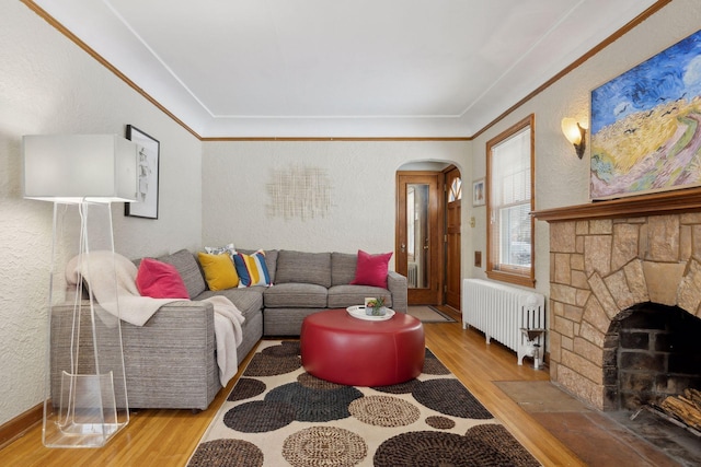 living room featuring ornamental molding, wood-type flooring, a stone fireplace, and radiator