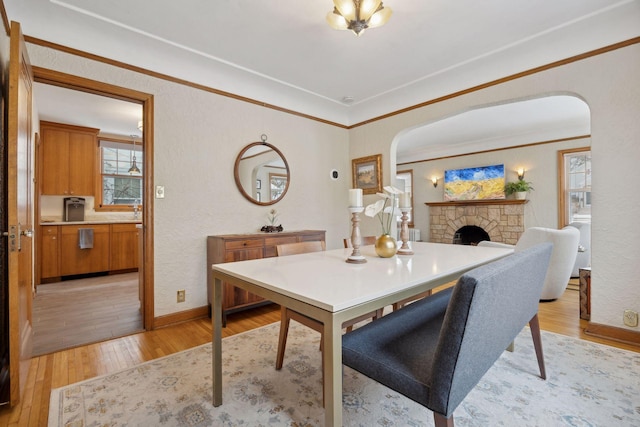 dining room featuring crown molding, a stone fireplace, and light hardwood / wood-style flooring