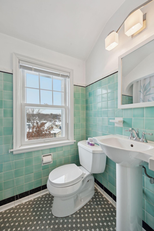 bathroom featuring lofted ceiling, tile patterned floors, toilet, and tile walls