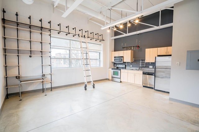 kitchen featuring appliances with stainless steel finishes, a towering ceiling, light brown cabinetry, sink, and electric panel