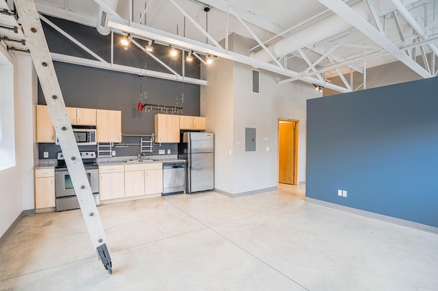 kitchen with light brown cabinetry, sink, light stone counters, appliances with stainless steel finishes, and a towering ceiling