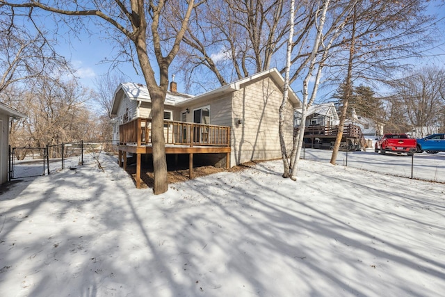 view of snowy exterior featuring a chimney, fence, and a wooden deck