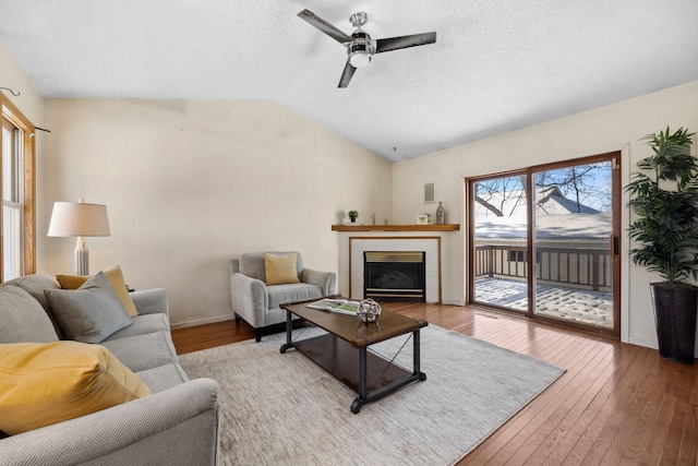 living room featuring a tile fireplace, lofted ceiling, ceiling fan, wood finished floors, and a textured ceiling