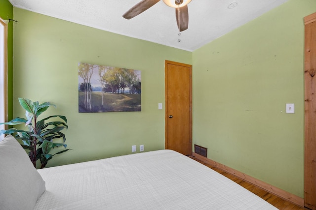 bedroom featuring baseboards, ceiling fan, visible vents, and wood finished floors