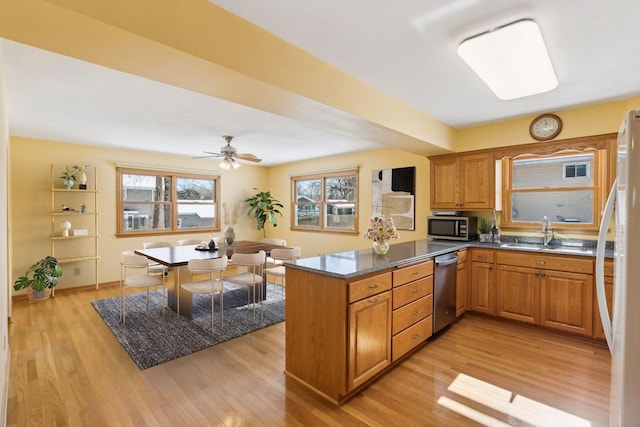 kitchen featuring a sink, light wood finished floors, stainless steel appliances, brown cabinetry, and a peninsula