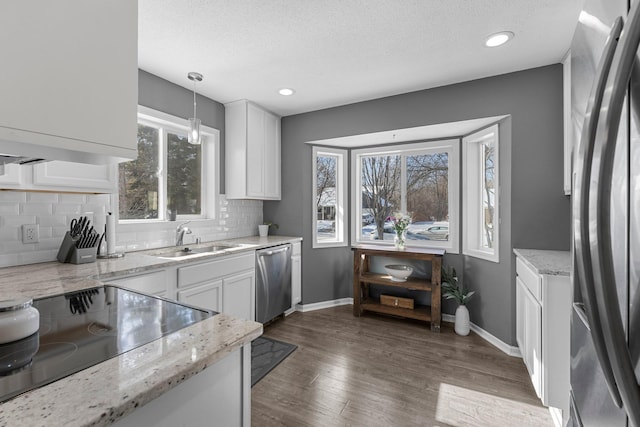 kitchen with appliances with stainless steel finishes, pendant lighting, white cabinetry, sink, and light stone countertops