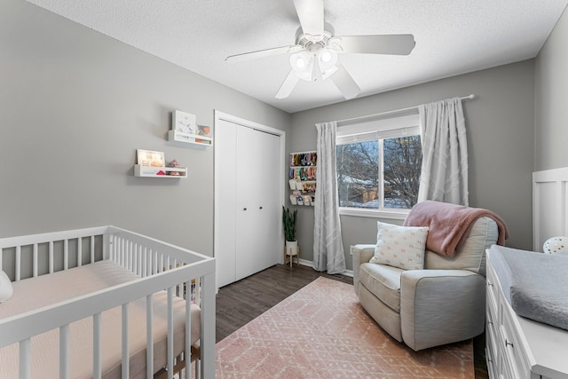 bedroom with a nursery area, dark hardwood / wood-style flooring, a closet, and a textured ceiling