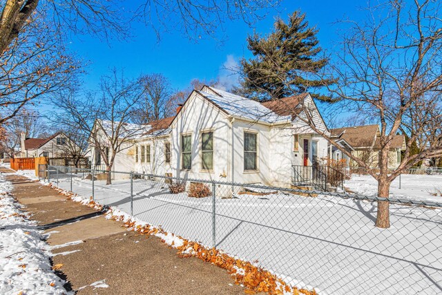 snow covered property featuring a fenced front yard, a residential view, and stucco siding