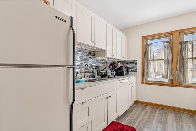 kitchen with tasteful backsplash, light countertops, white cabinetry, a sink, and white appliances