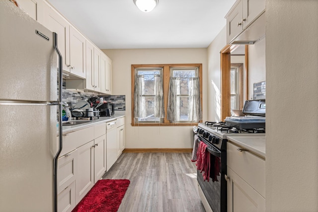 kitchen featuring tasteful backsplash, range with gas stovetop, light wood-style flooring, freestanding refrigerator, and light countertops