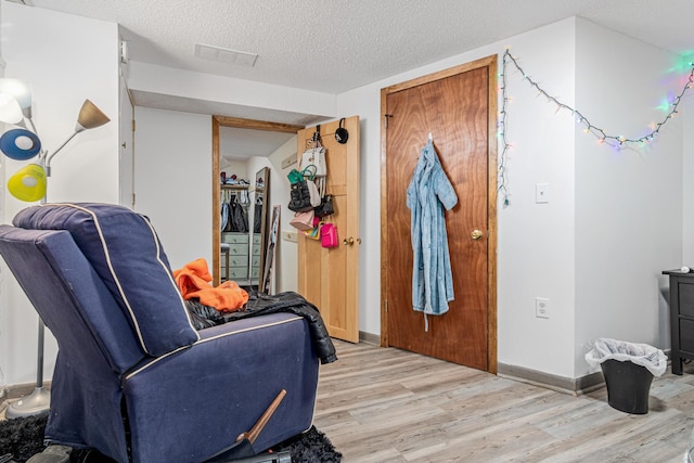 interior space with a textured ceiling, light wood finished floors, visible vents, and baseboards