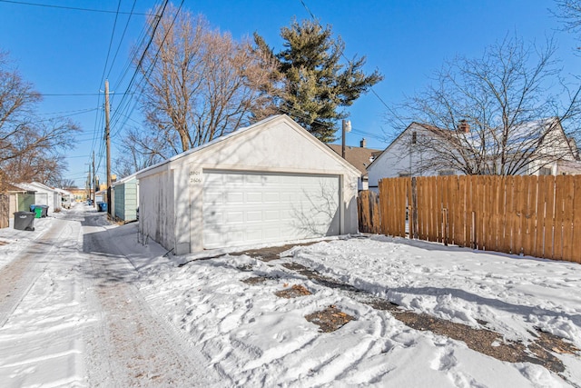 snow covered garage featuring a detached garage and fence