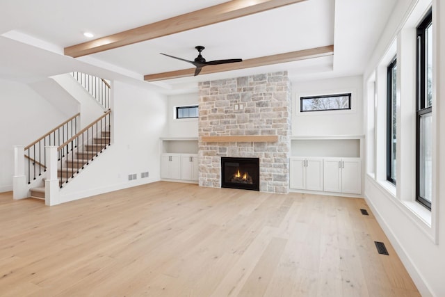 unfurnished living room with ceiling fan, a fireplace, beam ceiling, and light hardwood / wood-style floors