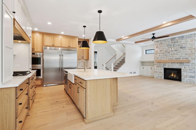 kitchen with sink, a kitchen island with sink, pendant lighting, stainless steel appliances, and light hardwood / wood-style floors