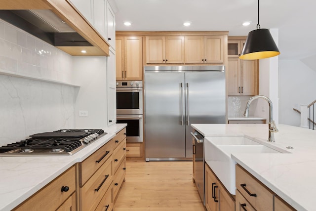 kitchen with premium range hood, decorative light fixtures, light stone counters, stainless steel appliances, and light wood-type flooring