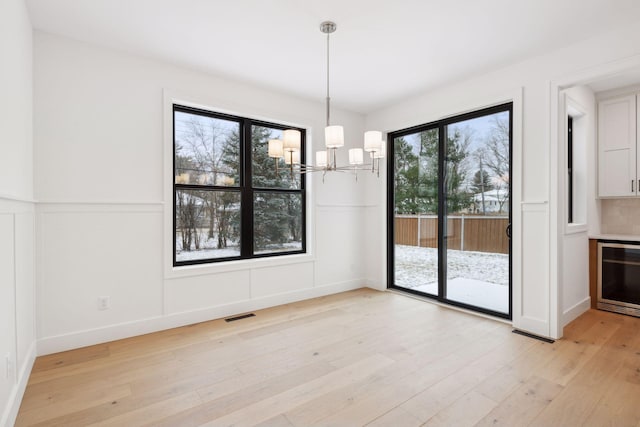 unfurnished dining area with an inviting chandelier, light hardwood / wood-style flooring, and beverage cooler