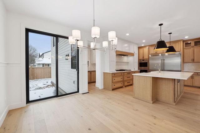 kitchen with pendant lighting, stainless steel appliances, tasteful backsplash, an island with sink, and light wood-type flooring