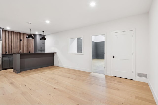 interior space featuring stainless steel refrigerator, a kitchen bar, hanging light fixtures, kitchen peninsula, and light hardwood / wood-style flooring