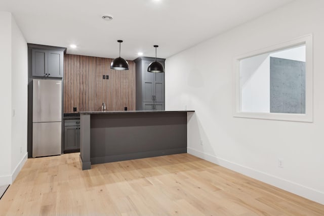 kitchen with stainless steel refrigerator, a kitchen breakfast bar, light hardwood / wood-style floors, decorative light fixtures, and kitchen peninsula