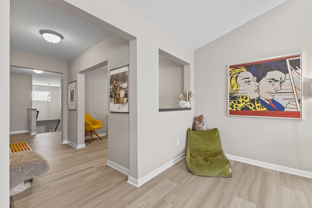 hallway with vaulted ceiling, a textured ceiling, and light hardwood / wood-style flooring