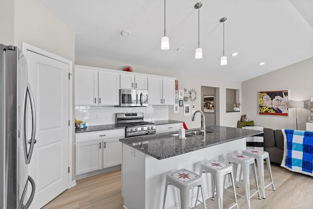 kitchen featuring appliances with stainless steel finishes, white cabinetry, sink, dark stone counters, and a center island with sink