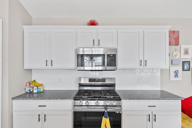 kitchen with stainless steel appliances, white cabinets, backsplash, and dark stone counters