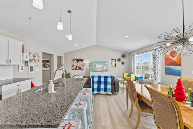 kitchen featuring sink, dark stone countertops, white cabinets, a center island with sink, and decorative light fixtures