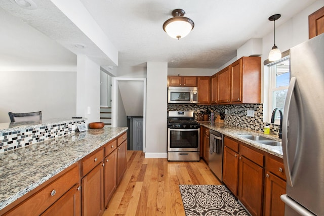 kitchen with sink, light stone counters, hanging light fixtures, light wood-type flooring, and stainless steel appliances