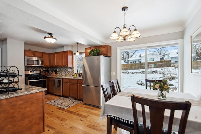 kitchen with pendant lighting, sink, stainless steel appliances, light stone countertops, and decorative backsplash