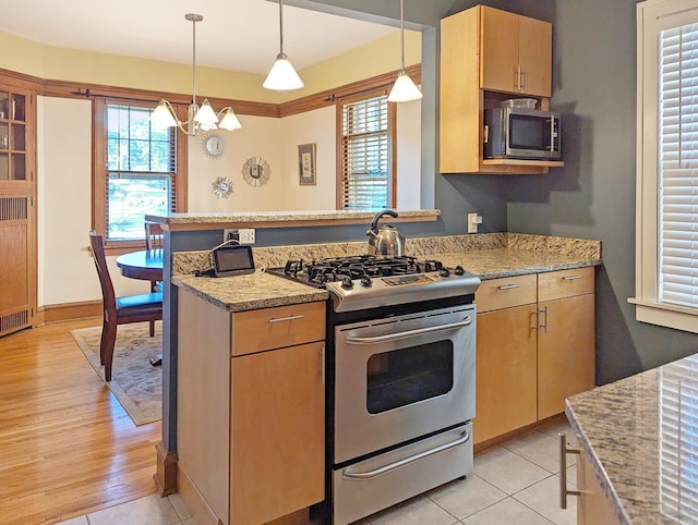 kitchen featuring hanging light fixtures, stainless steel appliances, a wealth of natural light, light stone countertops, and light brown cabinetry