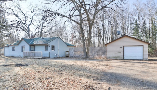 exterior space featuring an outbuilding, a detached garage, a chimney, a deck, and fence
