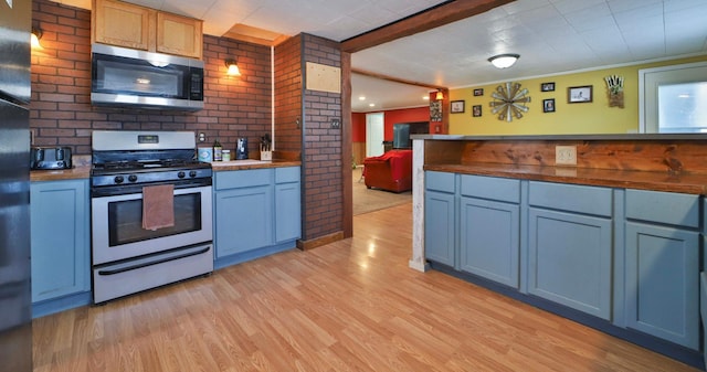 kitchen featuring beamed ceiling, stainless steel appliances, brick wall, light wood-style flooring, and blue cabinets