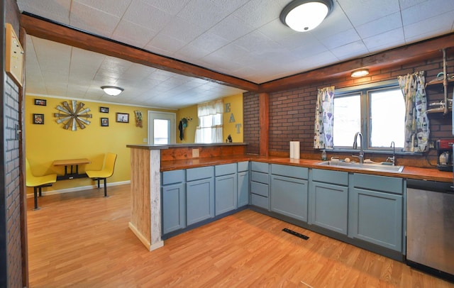 kitchen with light wood-style floors, a peninsula, stainless steel dishwasher, and a sink
