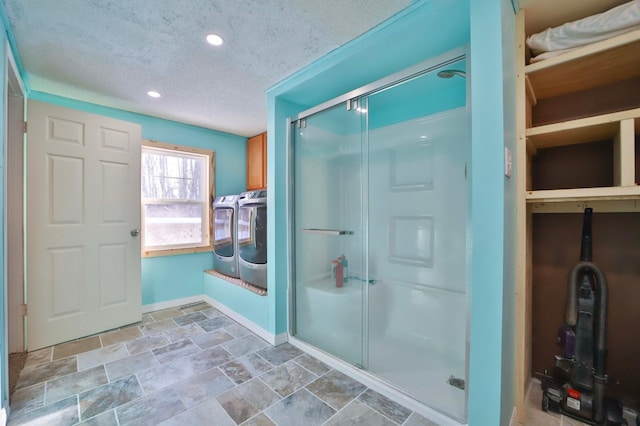 bathroom featuring washing machine and clothes dryer, stone finish flooring, baseboards, a stall shower, and a textured ceiling