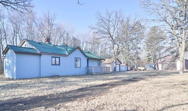 rear view of property with metal roof, an outdoor structure, a garage, and a chimney
