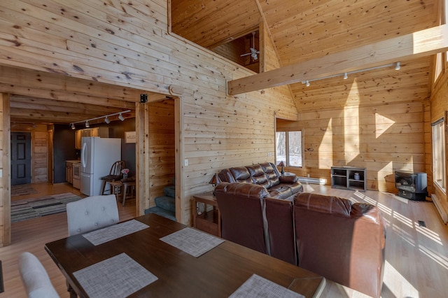 dining space with ceiling fan, wooden walls, high vaulted ceiling, track lighting, and light wood-type flooring