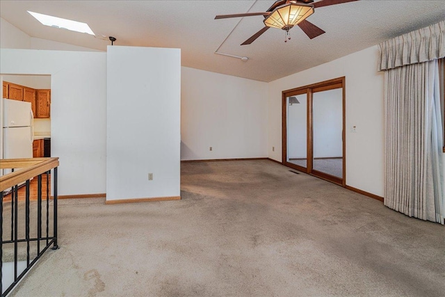 spare room with ceiling fan, light colored carpet, and vaulted ceiling with skylight